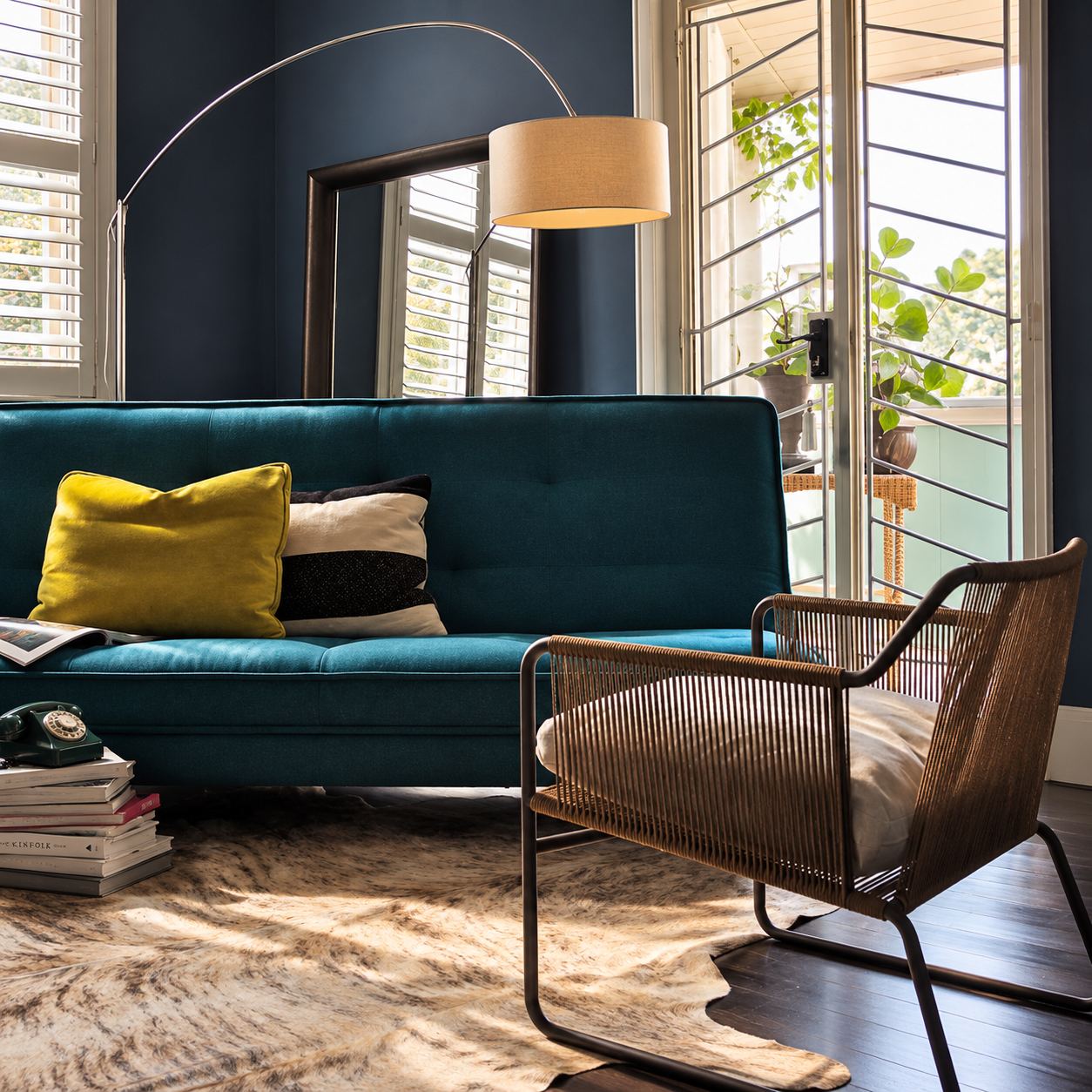 Teal sofa with yellow and striped cushions beside a rope armchair, a cowhide rug and shuttered windows in the Potts Point living room